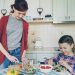 Happy mother and cheerful daughter cook salad together in the kitchen at home cutting vegetables and talking. Family, cooking, and people concept